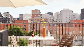 A balcony with two wooden chairs, a table with a bottle and glasses, and a large umbrella.