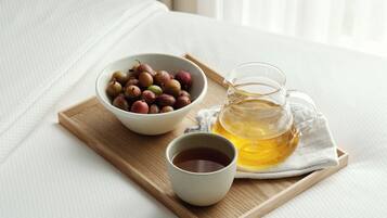 A wooden tray with a bowl of dried fruits, a glass pitcher of tea, and a cup of tea on a bed.