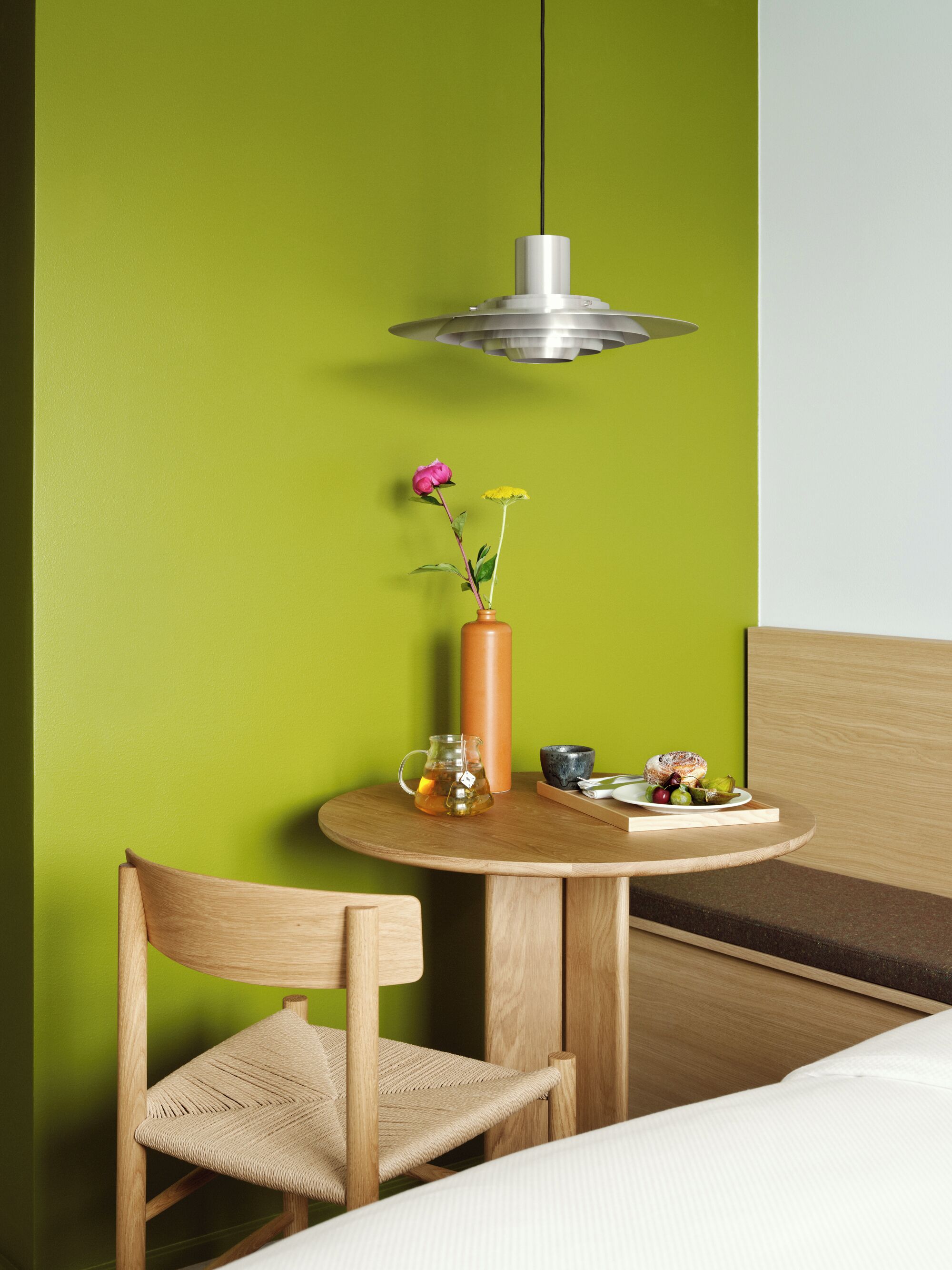 A room with a round wooden table, a vase with flowers, a pitcher, and a plate with food.
