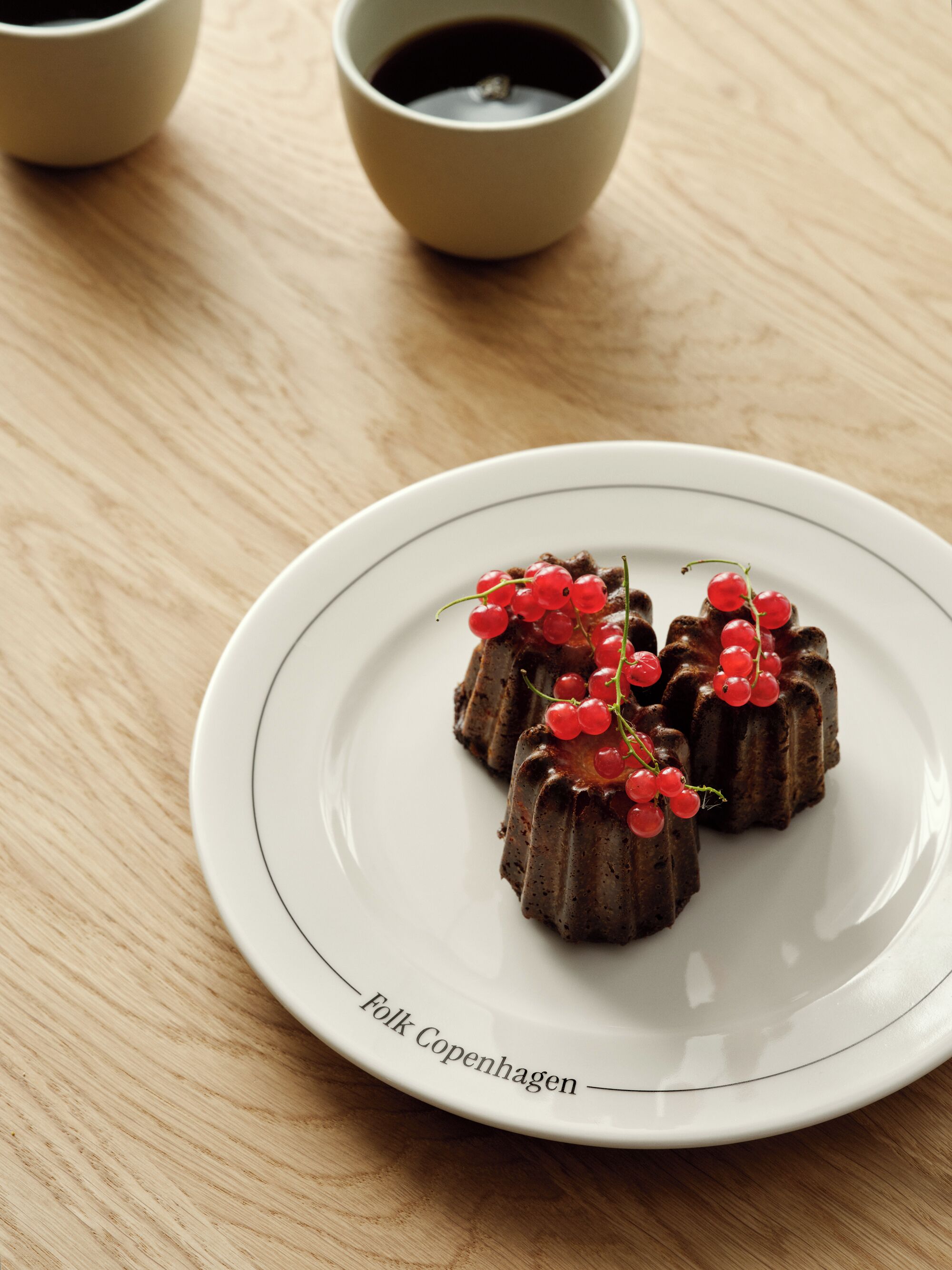 Um prato com três sobremesas de chocolate, decoradas com groselhas vermelhas, sobre um prato branco com borda.