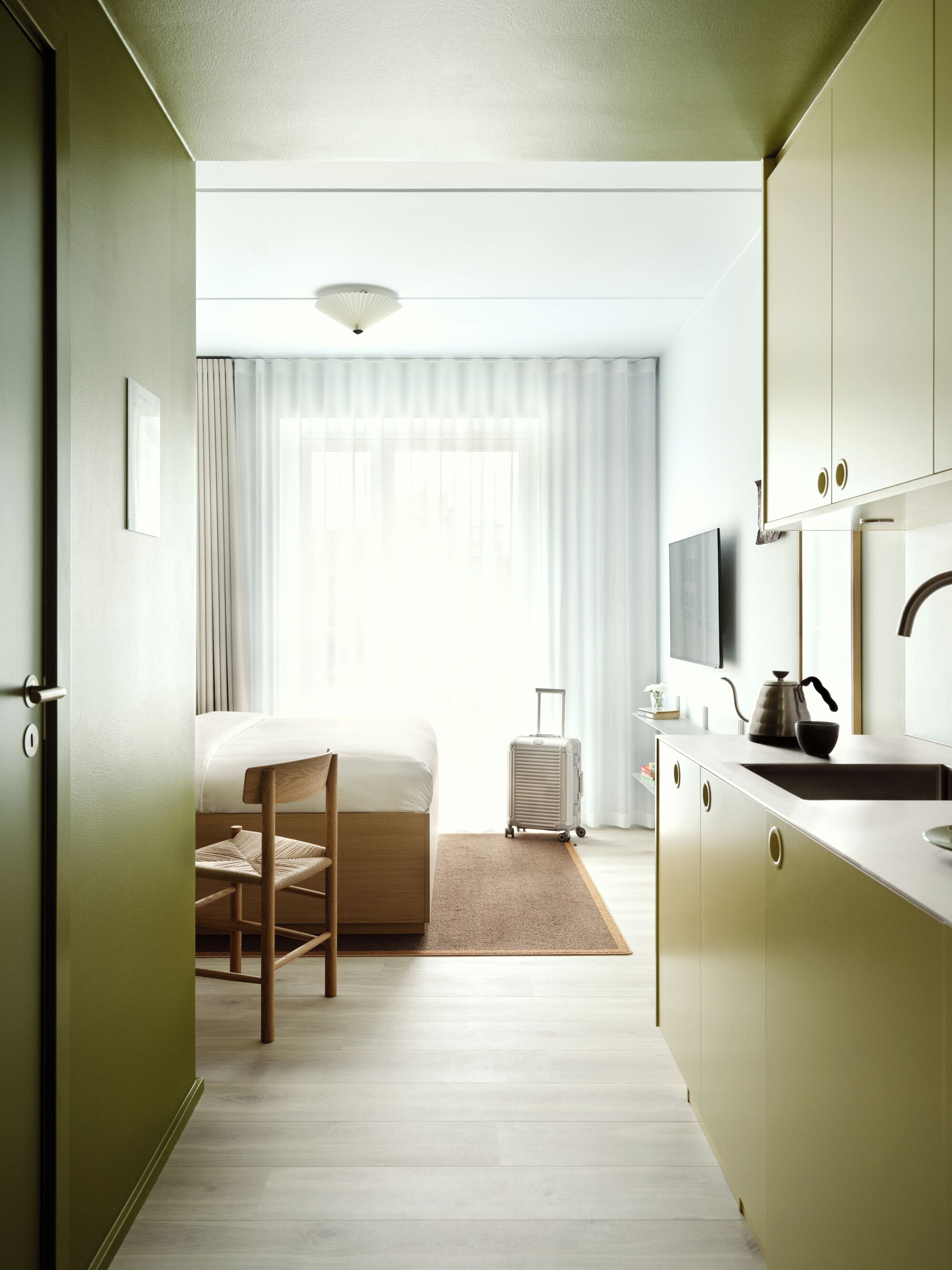 Una habitación de hotel con cama, una silla, una maleta, un área de cocina y un televisor.