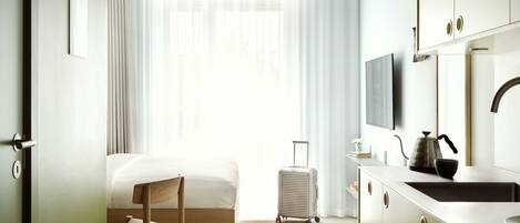 Una habitación de hotel con cama, una silla, una maleta, un área de cocina y un televisor.