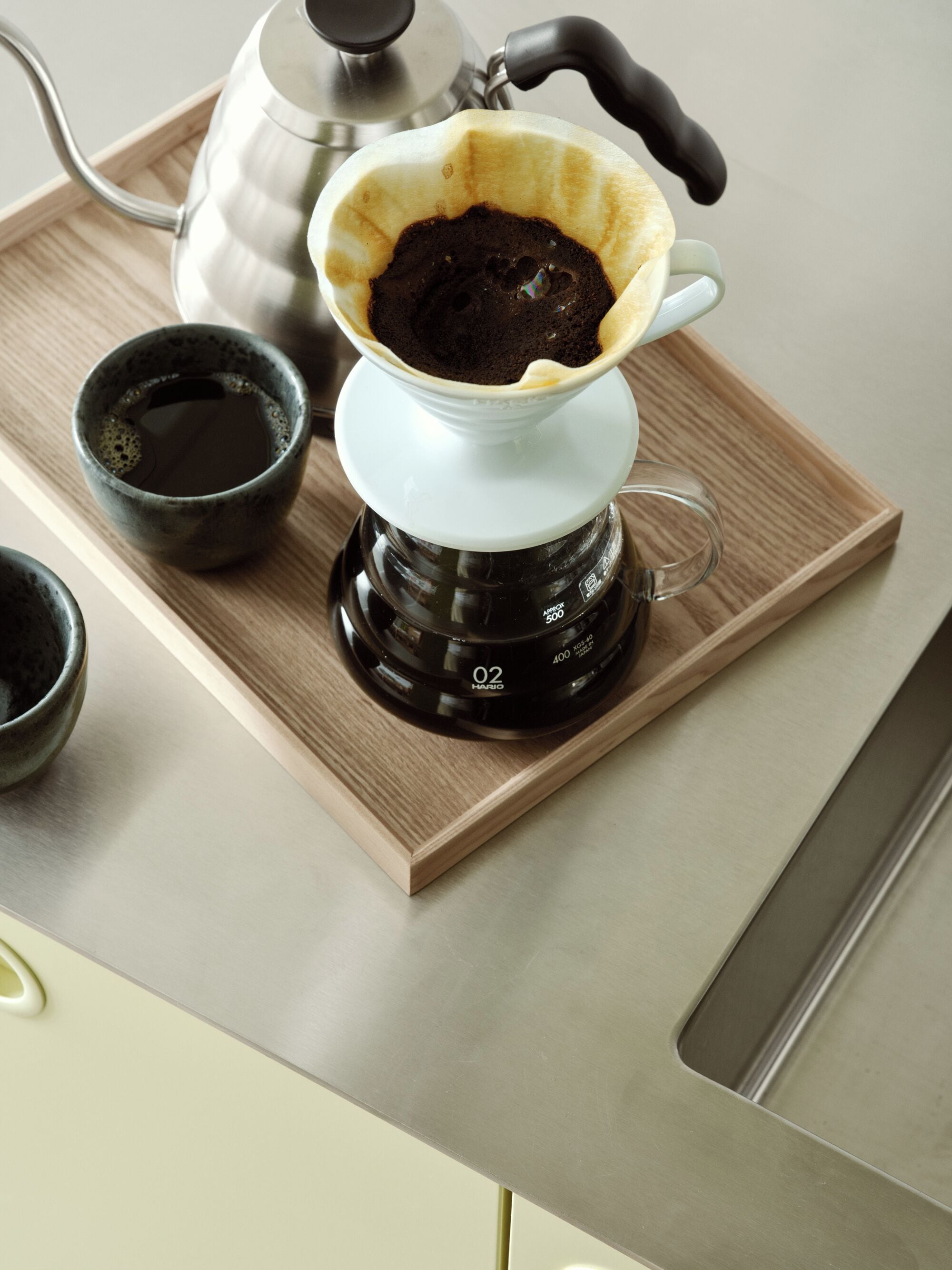 A coffee maker with a cup of coffee on a wooden tray.