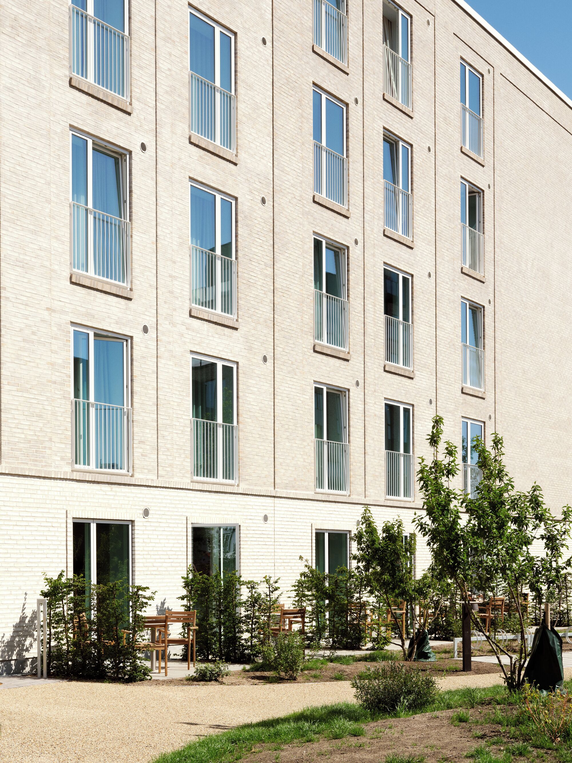 A multi-story building with a brick facade, large windows with white frames, and a courtyard with greenery and outdoor seating.