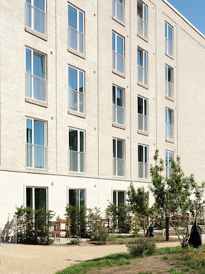 A multi-story building with a brick facade, large windows with white frames, and a courtyard with greenery and outdoor seating.