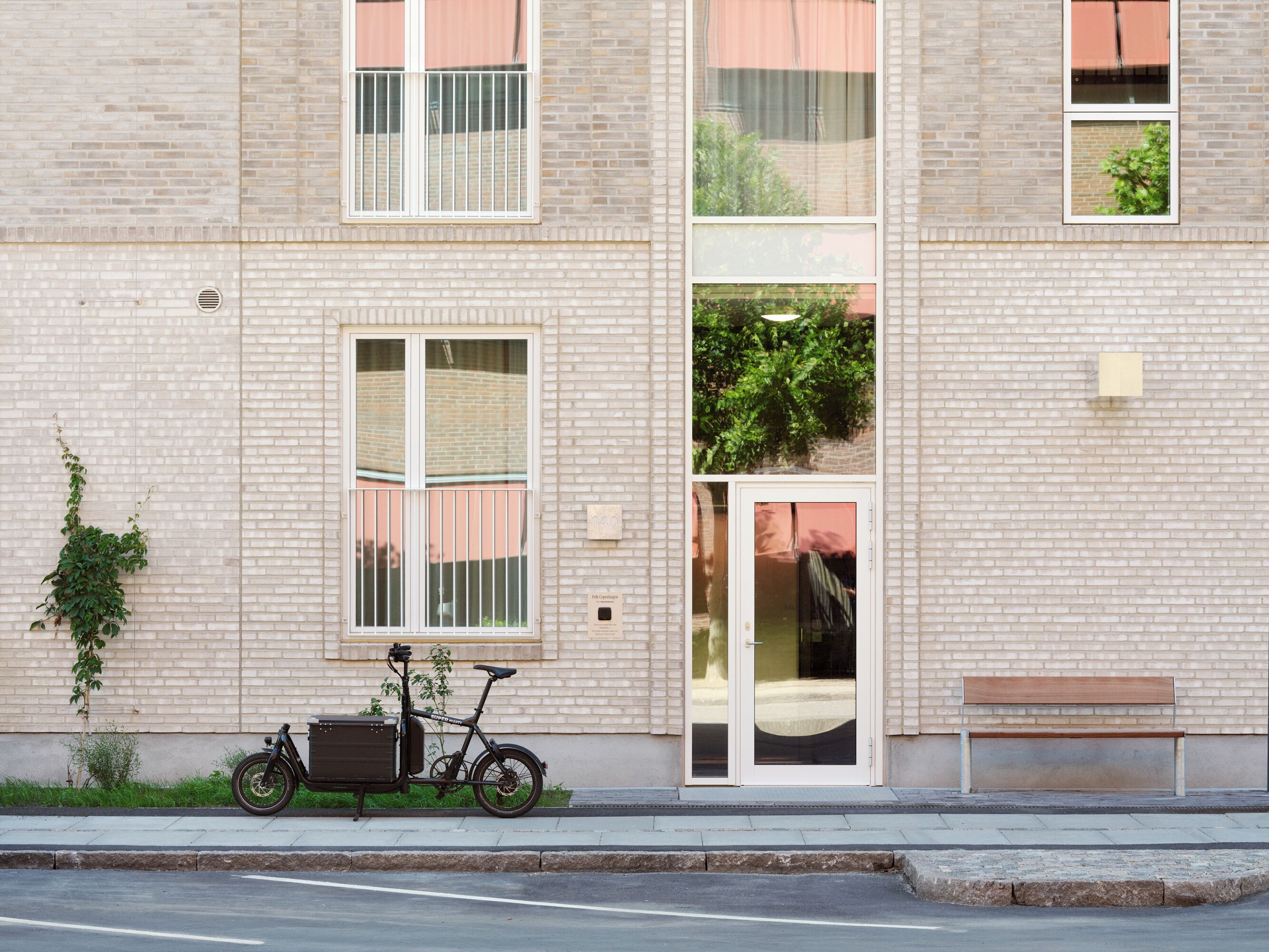 A building with a brick facade, a bicycle parked outside, and a bench on the sidewalk.