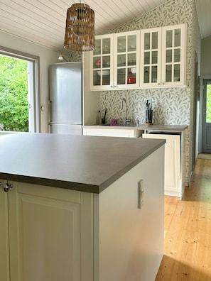 A kitchen with white cabinets, a large island, and a hanging light fixture. - Summer house on nature plot near Lynæs (Hundested)