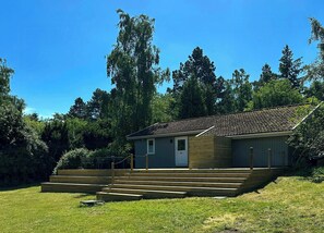 Ett litet trähus med ett tak täckt av takpannor, en ytterdörr och en trappa med trästeg som leder upp till entrén.