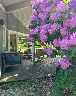En træterrasse med en stol og et bord, omgivet af lilla blomster.