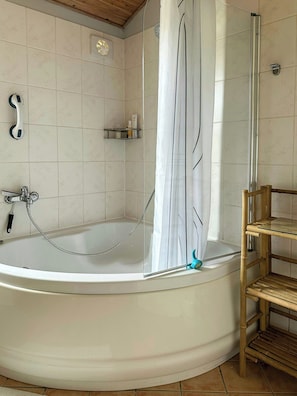A bathroom with a bathtub, a shower, a handrail, and a shelf with toiletries. - Summer house on nature plot near Lynæs (Hundested)