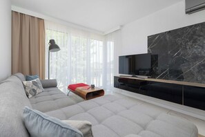Ein modernes Wohnzimmer mit grauem Sofa, einem Flachbildfernseher und einer Wand mit Marmorverkleidung.