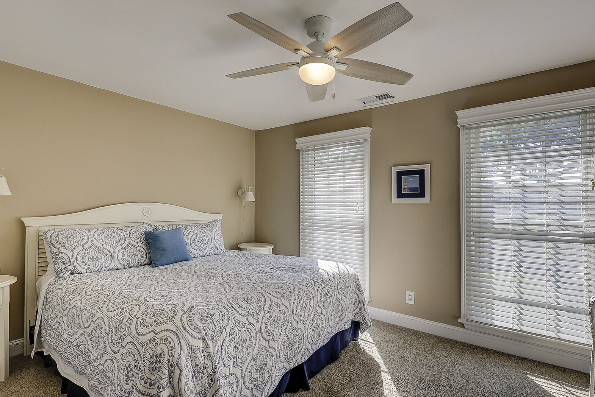 A bedroom with a bed, a ceiling fan, a nightstand, a lamp, and a window with blinds.