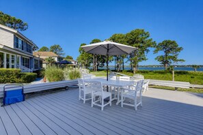 Une terrasse avec une table et des chaises, donnant sur un plan d’eau et une maison.