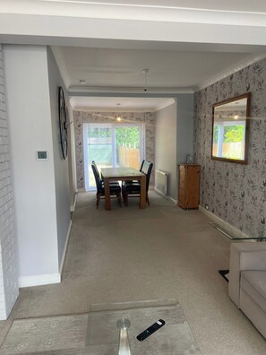 A dining area with a table and chairs, a clock, a radiator, and a window with a view of greenery. - London Charm - 3 Bedroom House (London)