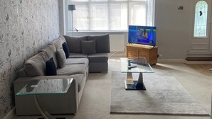 A living room with a sofa, a glass coffee table, a television, and a window with blinds. - London Charm - 3 Bedroom House (London)