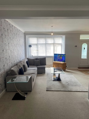 A living room with a sofa, a glass coffee table, a television, and a window with blinds. - London Charm - 3 Bedroom House (London)