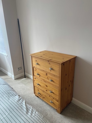 A wooden chest of drawers in a room with a carpeted floor and a window with blinds. - London Charm - 3 Bedroom House (London)
