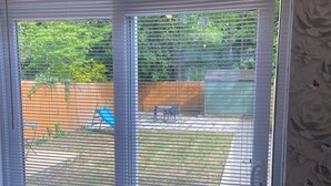 A room with a wooden table and chairs, a sliding glass door leading to a backyard with a fence, a lawn, and a tree. - London Charm - 3 Bedroom House (London)