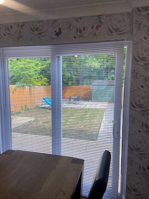 A room with a wooden table and chairs, a sliding glass door leading to a backyard with a fence, a lawn, and a tree. - London Charm - 3 Bedroom House (London)