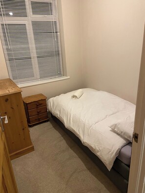 A bedroom with a single bed, a wooden dresser, and a window with blinds. - London Charm - 3 Bedroom House (London)