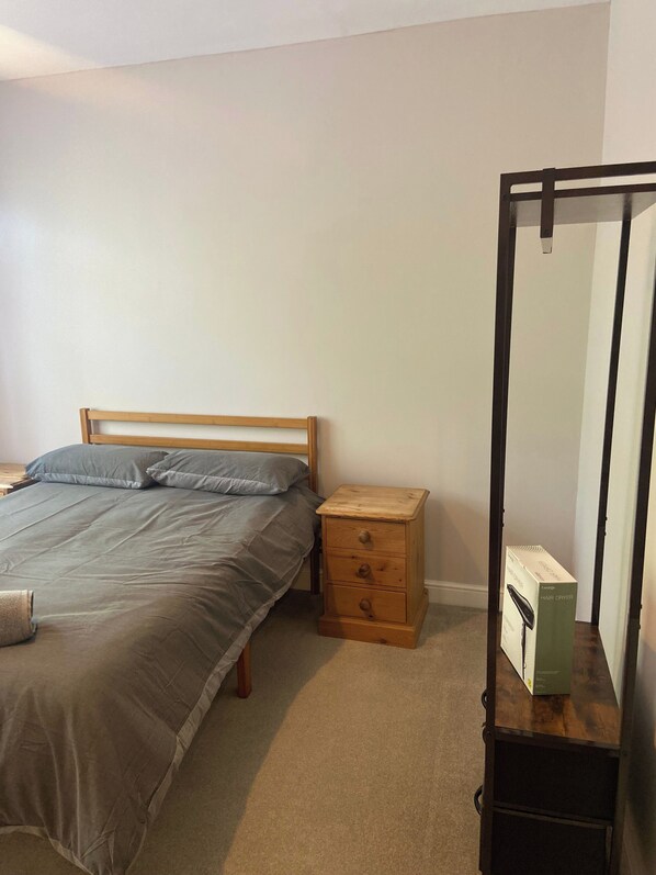 A bedroom with a bed, a wooden nightstand, a mirror, and a hair dryer box. - London Charm - 3 Bedroom House (London)