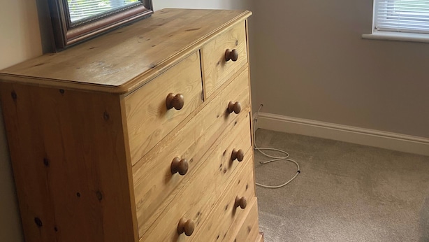 A wooden dresser with drawers and knobs, a framed picture leaning against the wall, and a window with blinds. - London Charm - 3 Bedroom House (London)