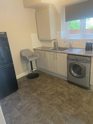 A compact kitchen with a built-in washing machine, a sink, and a refrigerator. - London Charm - 3 Bedroom House (London)