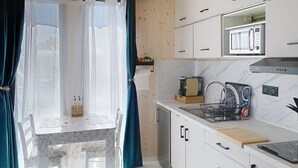 Eine moderne Küche mit integriertem Mikrowellenherd, einer Kaffeemaschine und einer Espressomaschine. Ein Esstisch mit Stühlen und ein Fenster mit Vorhängen sind ebenfalls vorhanden.