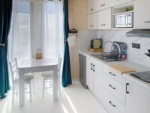 Una cocina moderna equipada con microondas, cafetera y máquina de espresso. Cuenta con una mesa de comedor con sillas y un ventanal con cortinas.