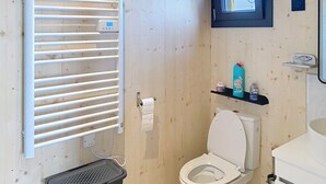 Ein Badezimmer mit Toilette, Handtuchhalter, Ablagefach für Pflegeprodukte und Wäschekorb.