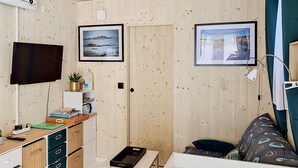 Ein gemütlicher Raum mit Fernseher, Holzwänden, einem Schreibtisch mit Schubladen, einem kleinen Tisch und zwei gerahmten Bildern.
