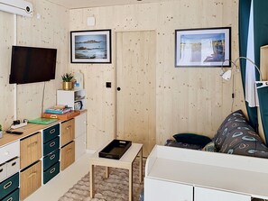 Habitación compacta con televisión, paredes de madera, un escritorio con cajones, una mesita y dos cuadros enmarcados.