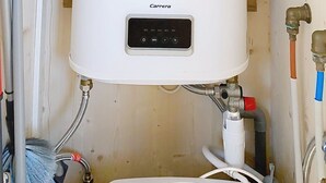 Ein weißer Warmwasserbereiter mit Bedienfeld, umgeben von verschiedenen Rohren und Schläuchen.