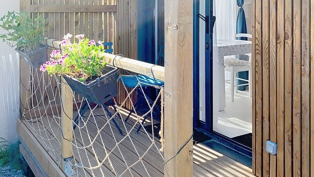 Eine Holzterrasse mit Seilbarriere, einem Blumentopf mit Blumen und einem Blick in einen Innenraum mit einer Tür.
