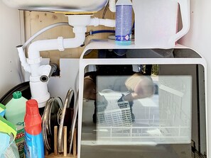 Una cocina compacta con un lavamanos, un sistema de filtración de agua y un espacio de almacenamiento con productos de limpieza.