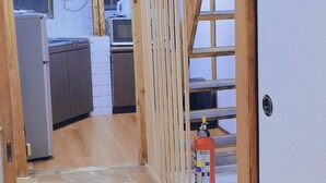 Een kamer met houten vloer, een schuifdeur, een keukenhoek met een magnetron en een ventilator.