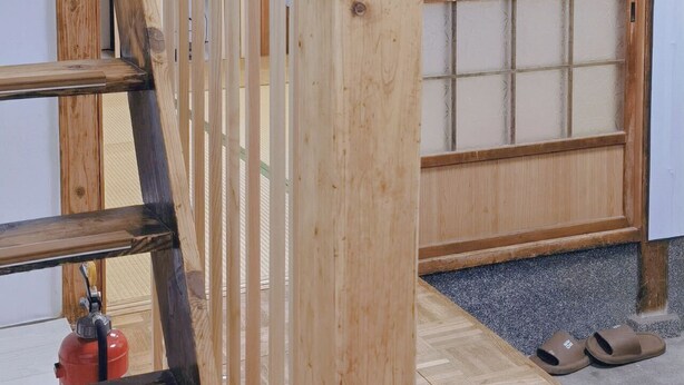 Een houten trap met een leuning, een rood brandblusapparaat en een houten vloer.