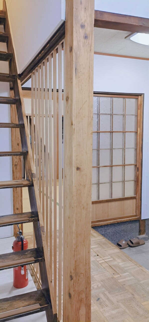 A wooden staircase with a handrail, a red fire extinguisher, and a wooden floor.