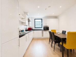 A modern kitchen with white cabinets, a black countertop, and a dining area with a table and chairs. - Free Underground Parking l 5 mins Wembley Stadium/Arena/Park Station (Wembley)