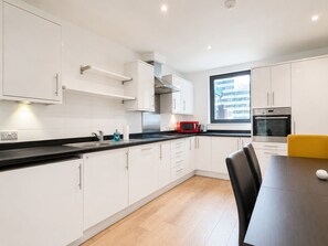 Une cuisine moderne avec des meubles blancs, un plan de travail noir, un micro-ondes rouge et une chaise jaune.