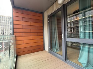 En balkon med trævæg, glasdør og udsigt til en bygning med stillads.