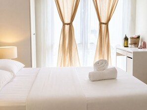 Quarto de hotel com cama, escrivaninha e janela com cortinas.
