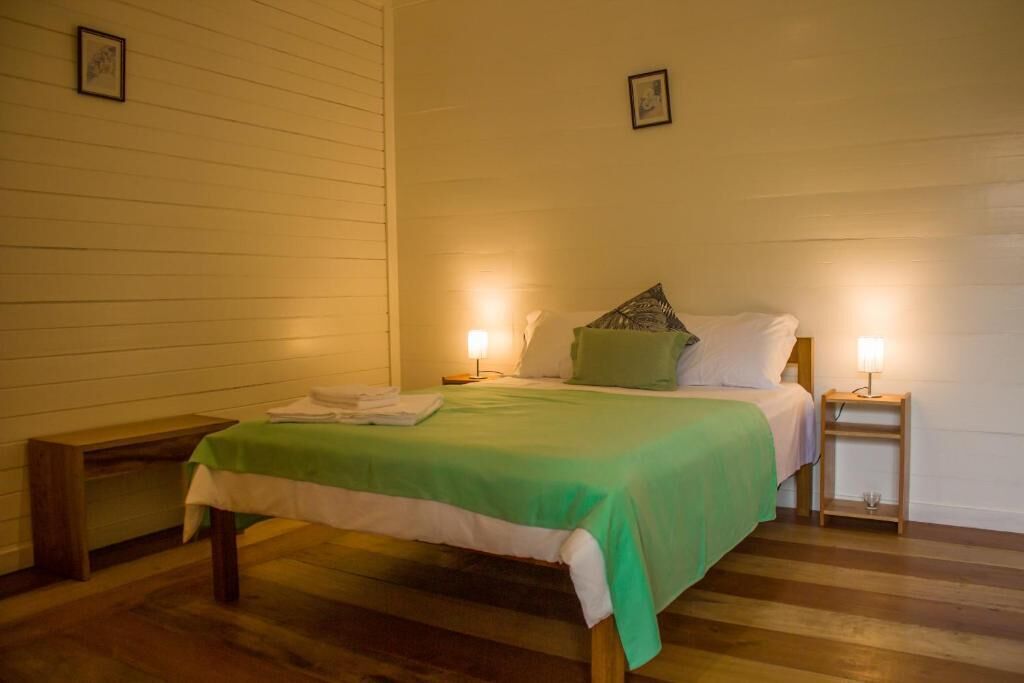 Een eenpersoonsbed met een groene sprei, twee bedlampjes en een houten nachtkastje.