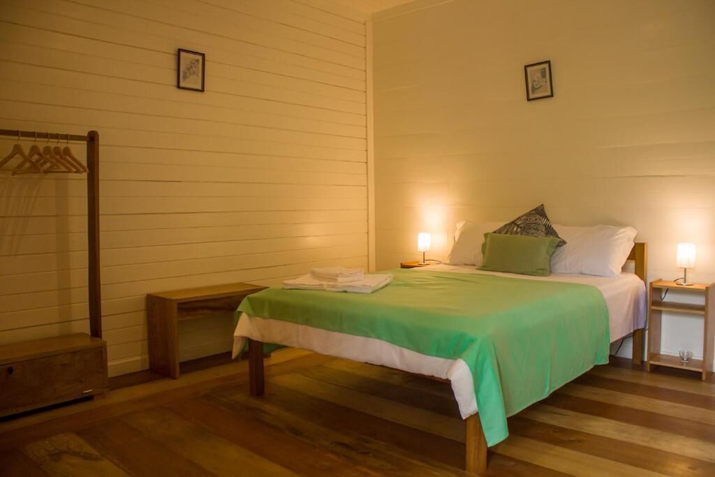 Um quarto com cama, abajures, um banquinho e um cabideiro.