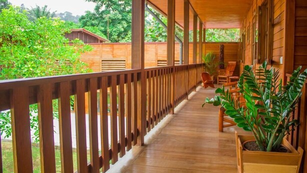 Une véranda en bois, recouverte et dotée d’une balustrade, agrémentée de plantes en pot et de mobilier d’extérieur.