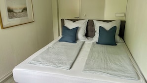 Een net opgemaakt bed met gestreept beddengoed, een ingelijst kunstwerk aan de muur en een deur op de achtergrond.