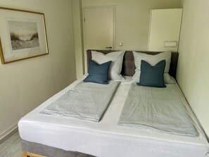 A neatly made bed with striped bedding, a framed picture on the wall, and a door in the background.