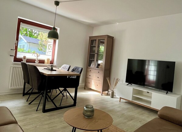 A living room with a dining table, chairs, a TV, a cabinet, and a window.