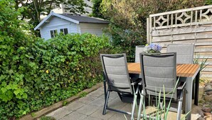 Een terras met een tafel en stoelen, omringd door groen en een houten hek.