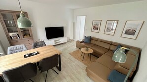 Een moderne woonkamer met een eethoek, een bank, een televisie en lijstwerken aan de muur.